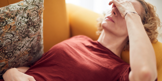 Frau liegt auf Sofa und deckt die Augen mit der Hand zu