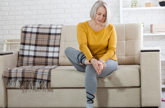 Frau sitzt auf Sofa und reibt sich den schmerzenden Fuß