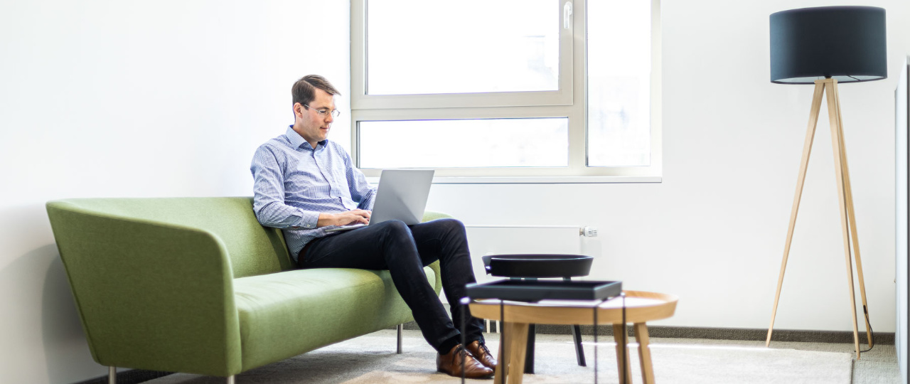 Mobiles Arbeiten in der GS28 Mitarbeiter sitzt mit Laptop auf dem Schoß auf dem Sofa